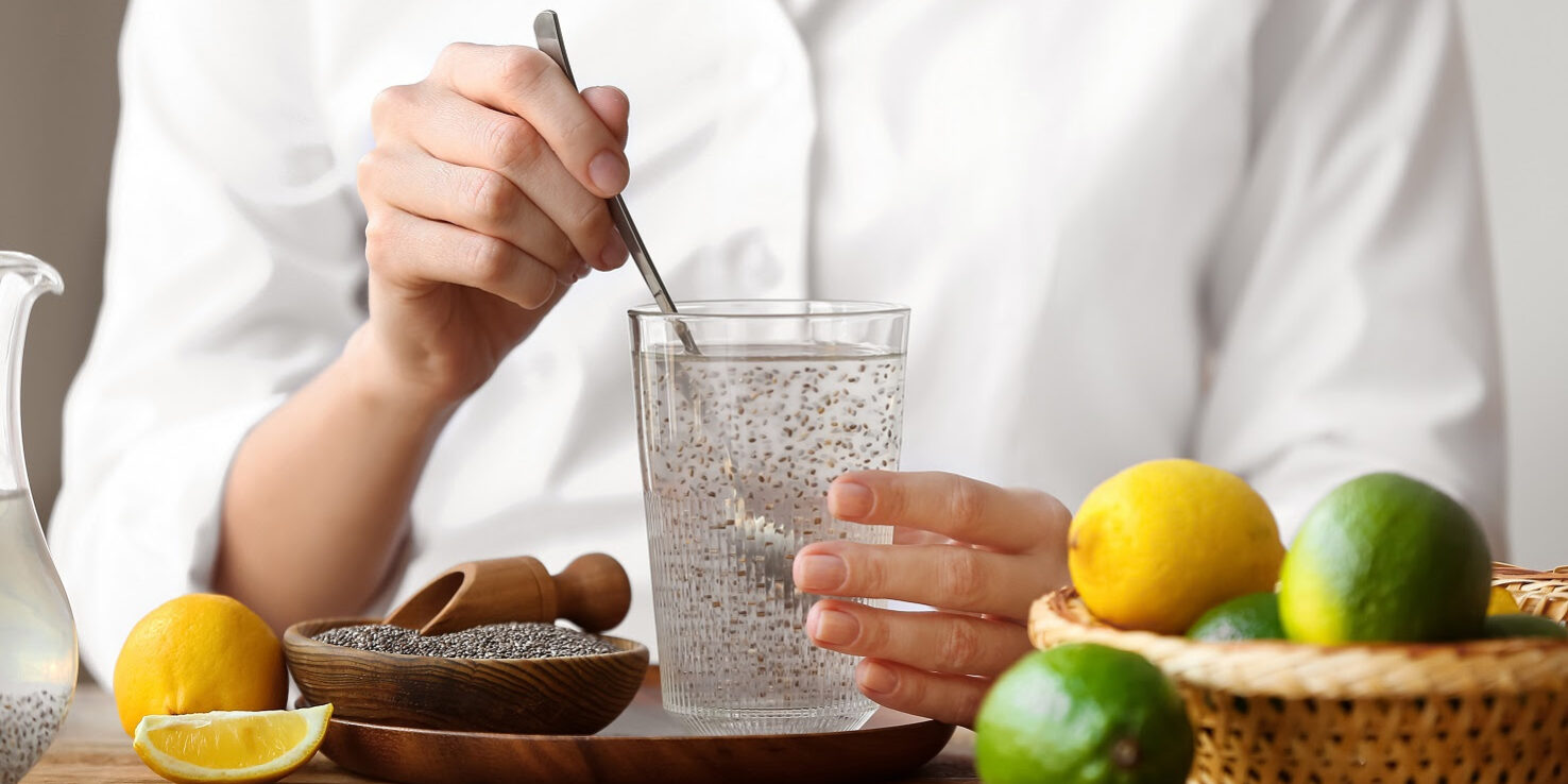 Woman stirring chia seeds in glass of water on wooden table with citrus fruits